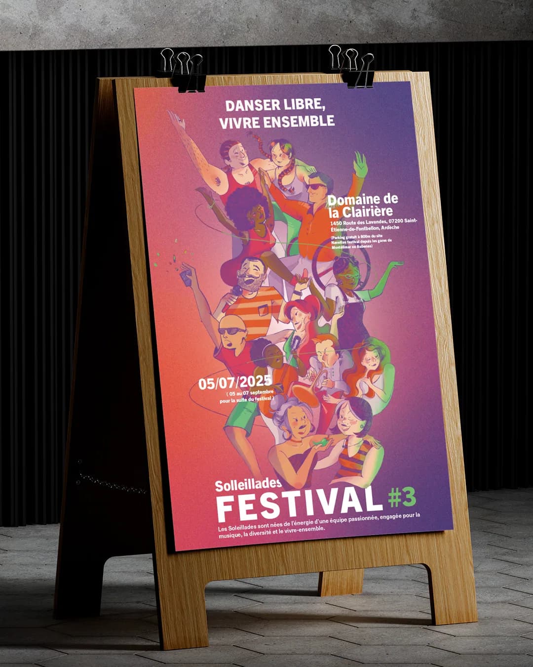 Mise en situation de l’affiche du festival Soleillades, tenue par deux pinces noires sur un chevalet en bois, dans une pièce sombre au sol carrelé.