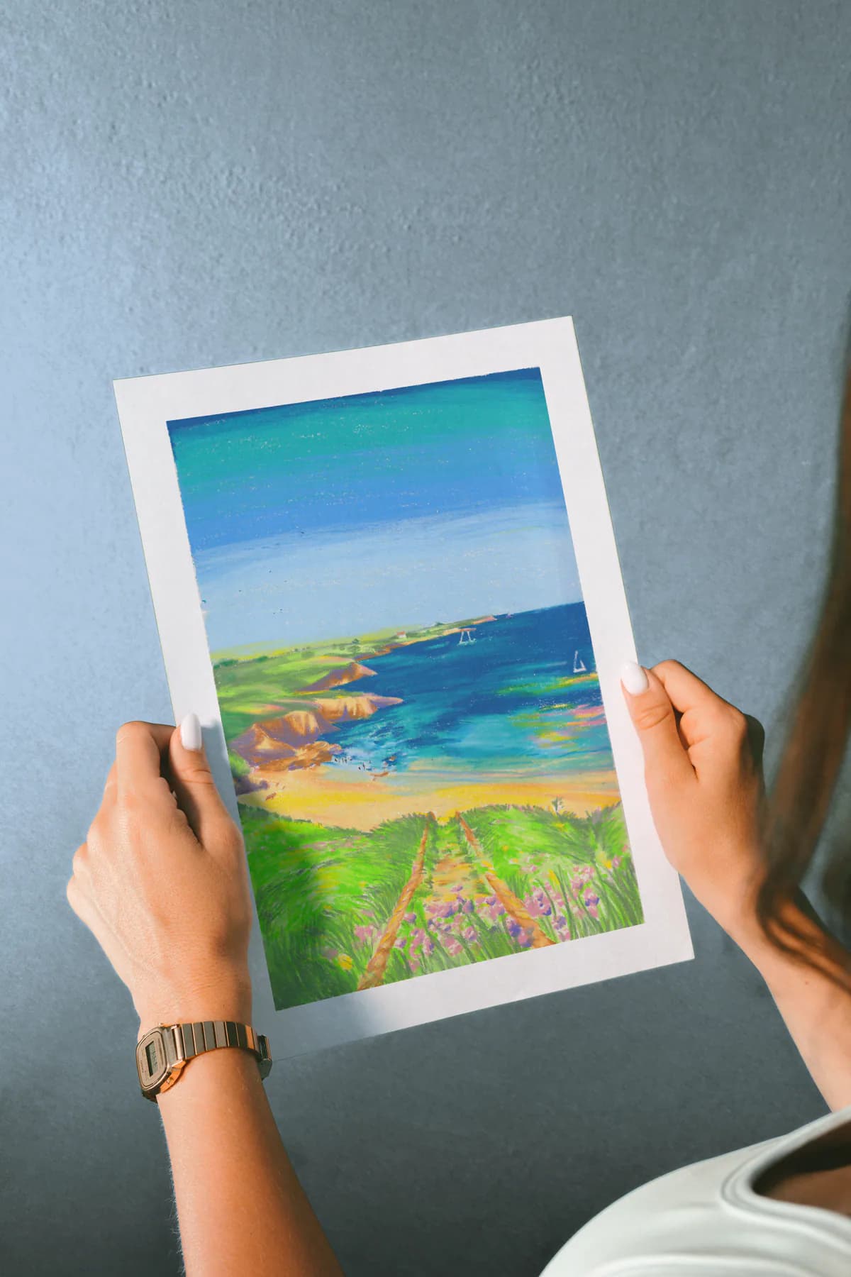 Le print Plage tenu à deux mains devant un mur bleu.